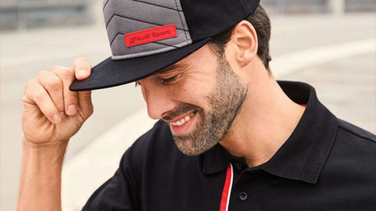 Un homme souriant en touchant sa casquette Audi.