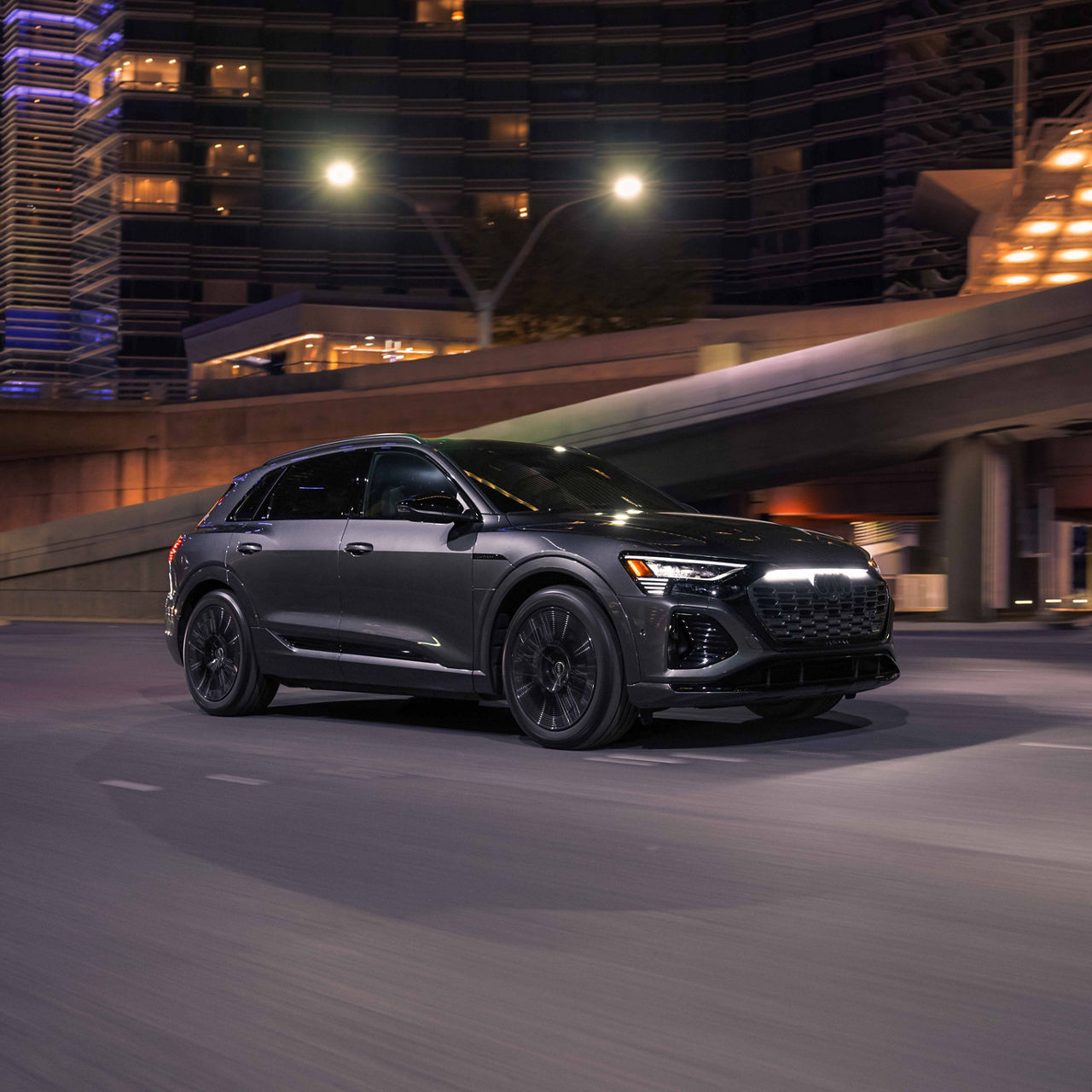 Un Audi Q8 e-tron gris passant sous un viaduc la nuit au centre-ville.