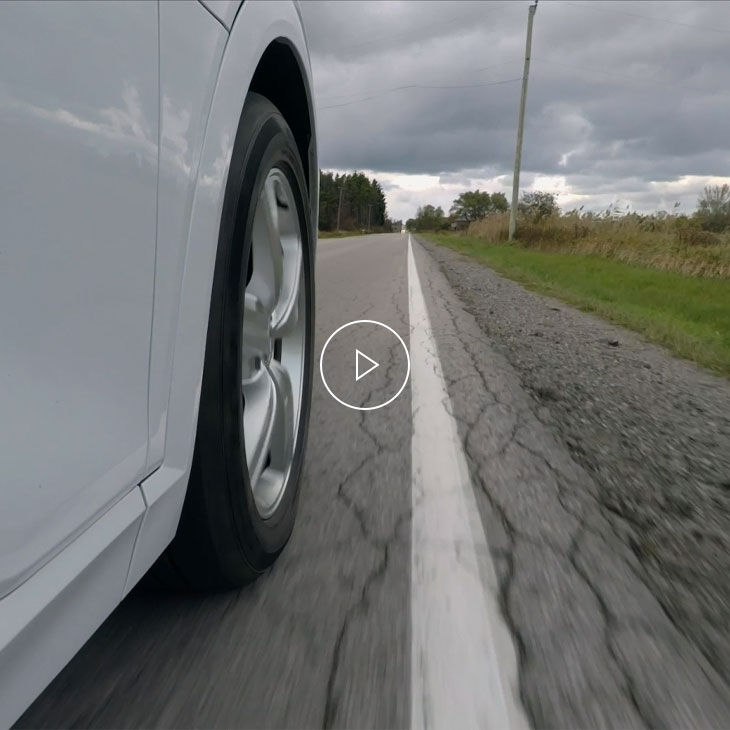 Gros plan de la roue d’un véhicule blanc en mouvement, près de la ligne peinte sur la route.