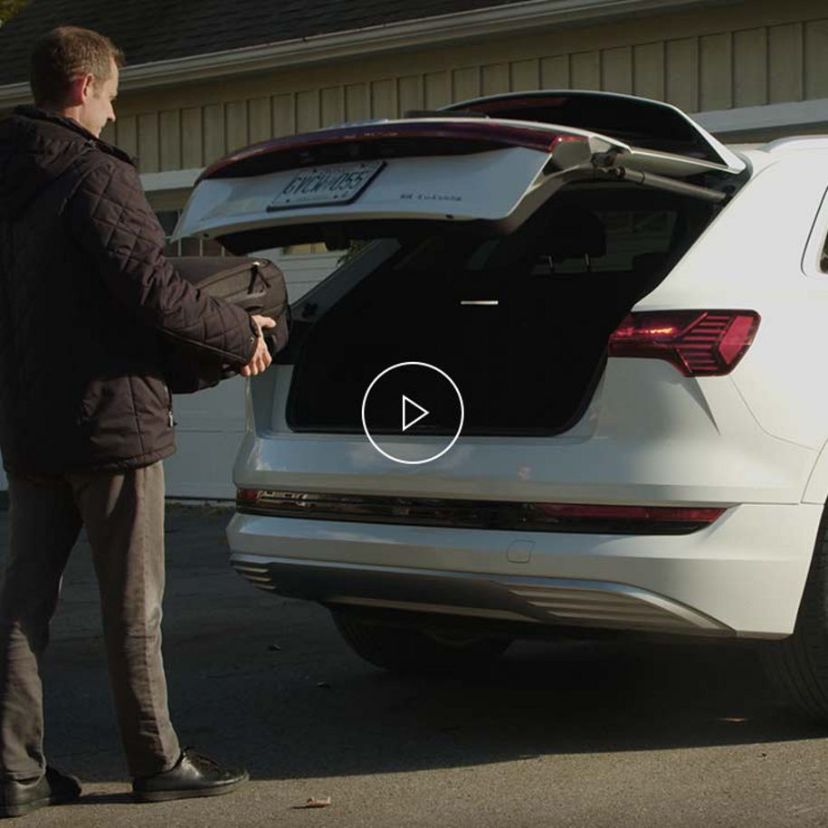 Photo of a person loading a suitcase into the hands-free luggage compartment of an Audi vehicle. 
