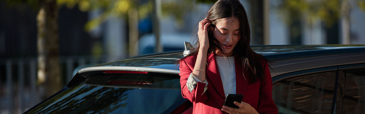 A woman standing in front of an Audi vehicle, looking down at her phone.