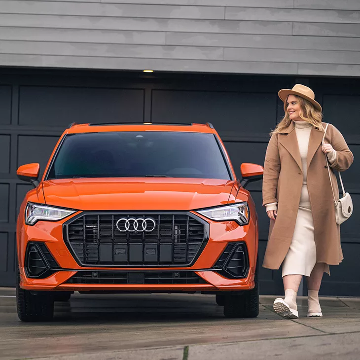 Femme debout à côté d’un VUS Audi orange stationné.