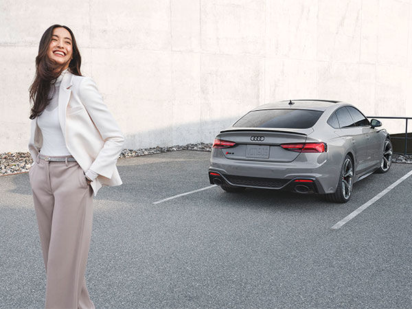A person standing and laughing with an Audi RS 5 Sportback parked in the background.