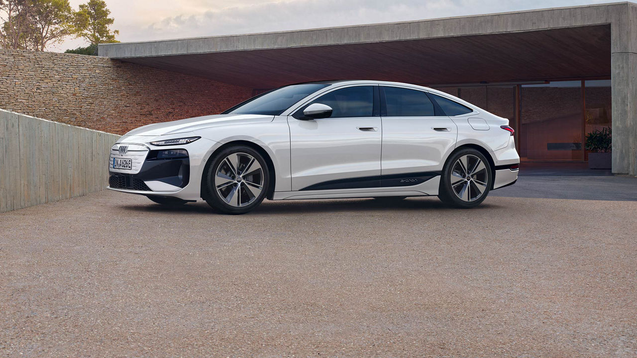 3/4 side profile of the Audi Q6 e-tron parked next to a modern house. 