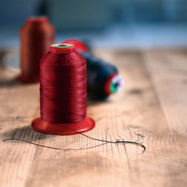 A spool of red thread resting on top of a wooden worktable.