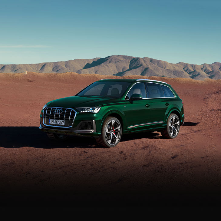 Three-quarter front view of a dark green Audi Q7 driving in the desert. 