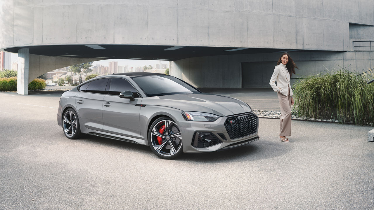 Woman standing left of a space-grey 2023 Audi RS5 Sportback.