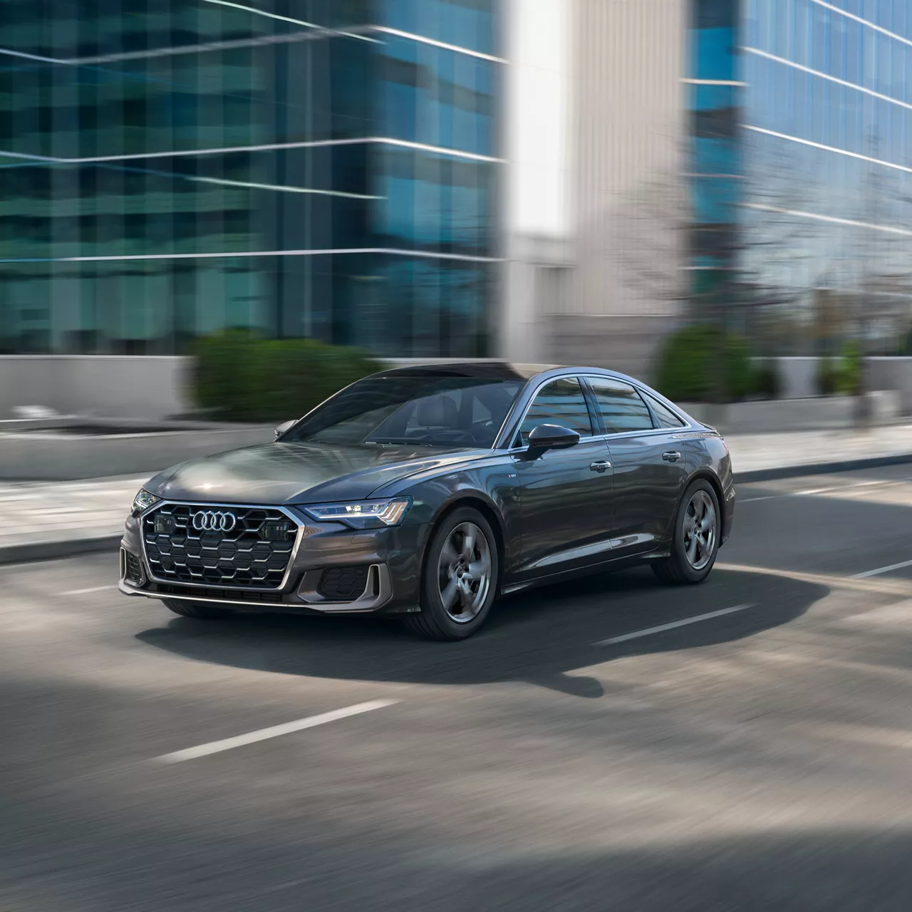 A black 2024 Audi A6 driving by an urban structure.