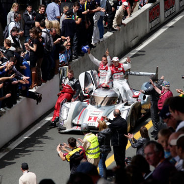  The team who won the 2012 "24 Hours of Le Mans" seated on top of the vehicle they drove as fans look on.  