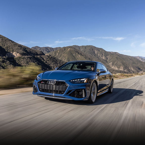 Front view of a blue Audi RS 5 Sportback driving on a mountain road.