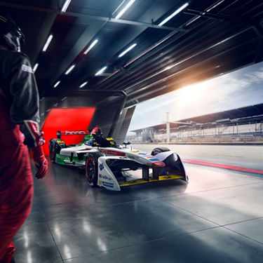  Three-quarter front view of an Audi Formula E vehicle parked in the pit stop of a racetrack. 