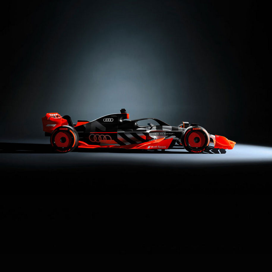 Vue latérale d’un véhicule de Formule 1 aux couleurs d’Audi stationné dans une salle d’exposition sombre.