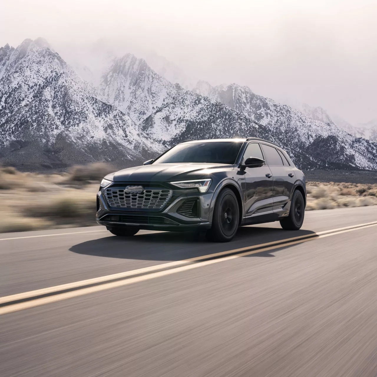 Three-quarter front view of a black Audi Q8 e-tron driving on a mountain road. 