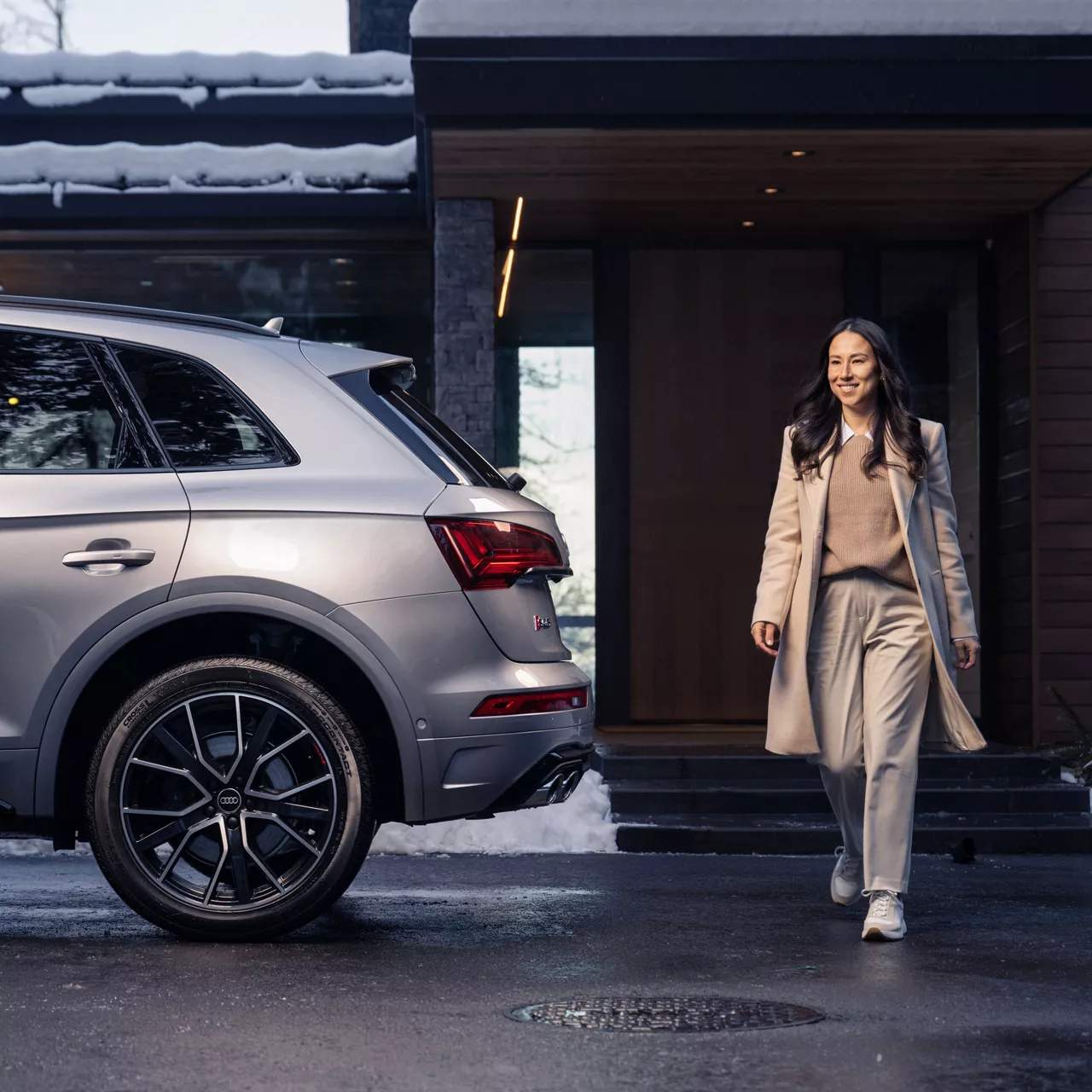 A woman smiling as she approaches her silver Audi SQ5. 