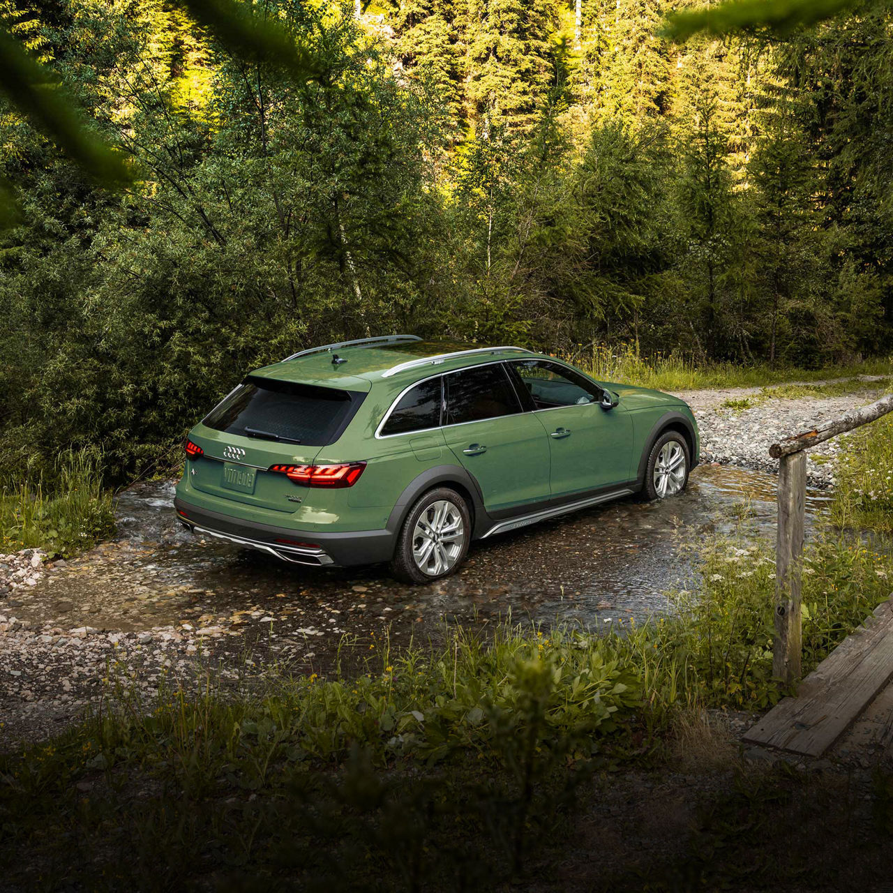 A green Audi A4 allroad crossing a large puddle on a gravel road. 