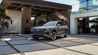 Three-quarter front view of a gray Audi Q4 e-tron parked in front of a modern building. 