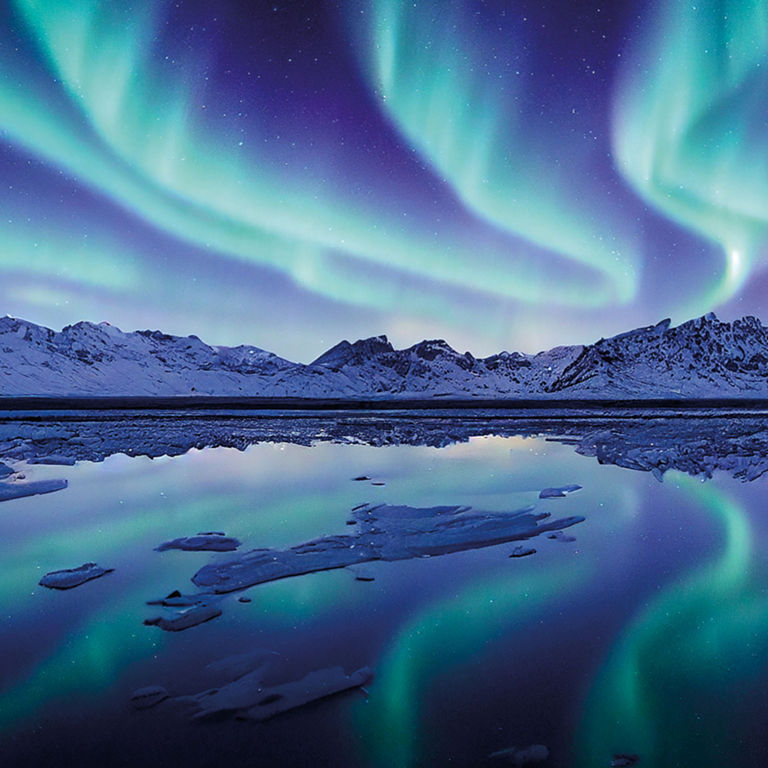 The aurora borealis in the sky shown against a background of snow-capped mountains.  