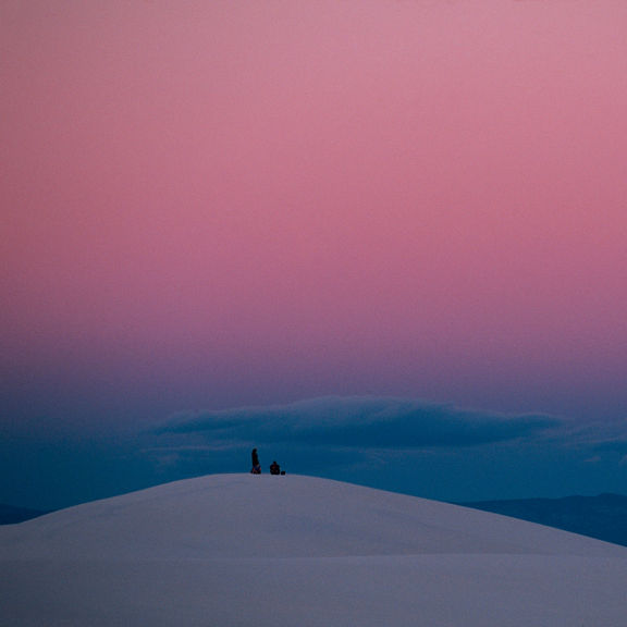 Two people standing atop a snowy hill overlooking a small town in valley below. 