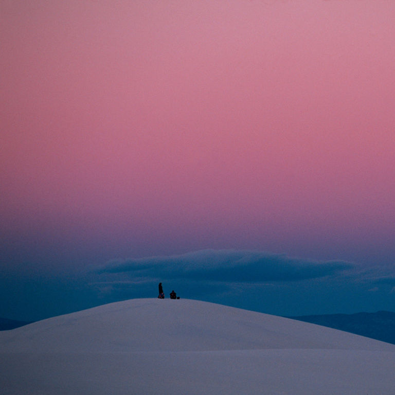 Two people standing atop a snowy hill overlooking a small town in valley below. 