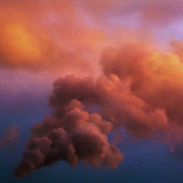 A plume of red and orange smoke against a blue sky.