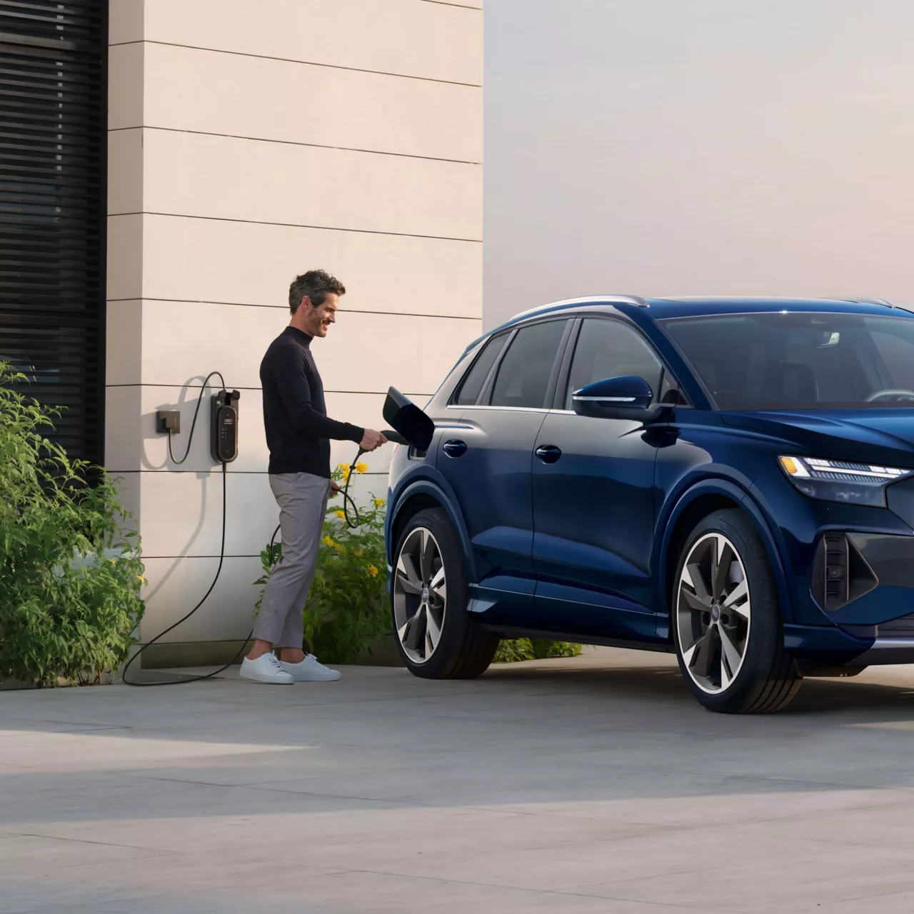 A man charging his Audi Q4 Sportback e-tron in front of a modern home.