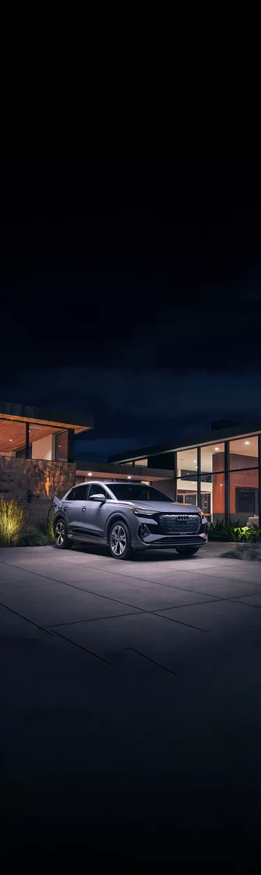 Un Audi Q8 e-tron argenté en recharge la nuit devant une maison moderne.