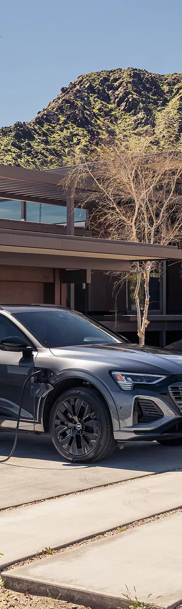 Side view of an Audi Q8 e-tron charging in front of a home. 