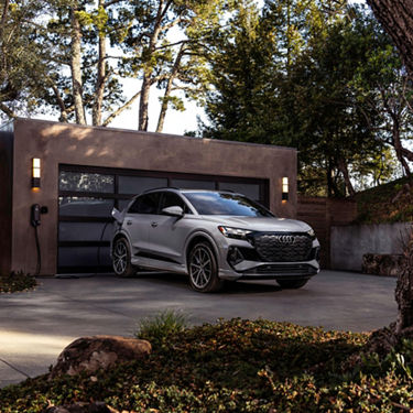 A silver Audi Q4 e-tron charging in front of a modern home. 