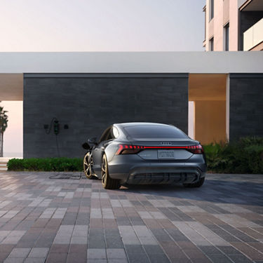 Rear view of a blue Audi e-tron GT charging in front of a modern building. 