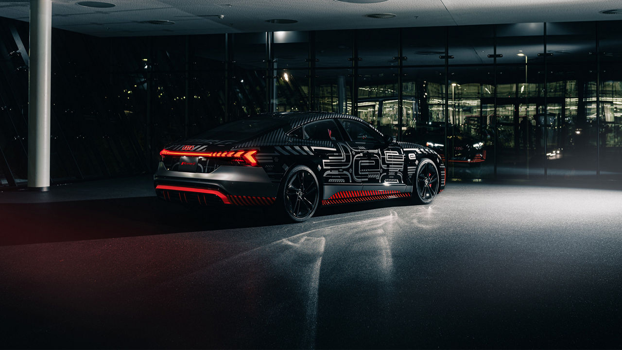 Three-quarter rear view of the Audi RS e-tron GT project 513/2 parked inside of a glass building at night. 