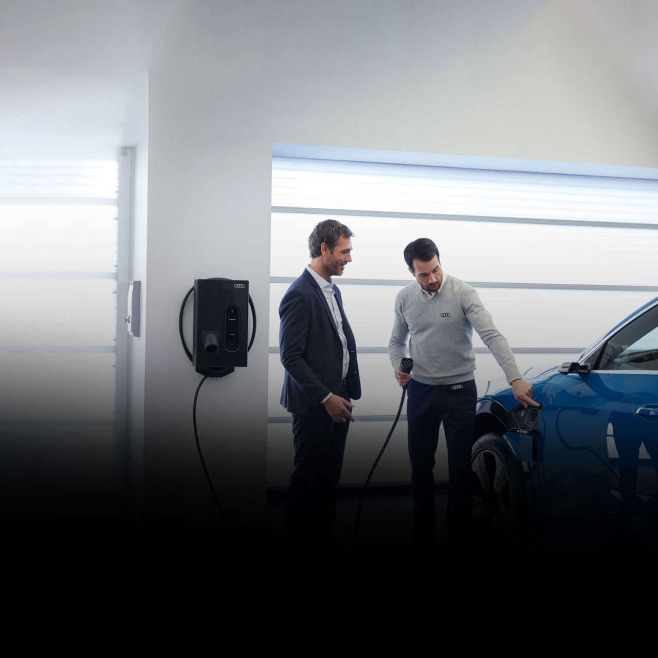 "An Audi dealer showing a customer how to charge his Audi e-tron vehicle. 																								"