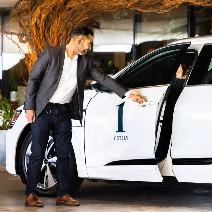 Side profile of a 1 Hotel representative helping someone out of their white Audi vehicle.