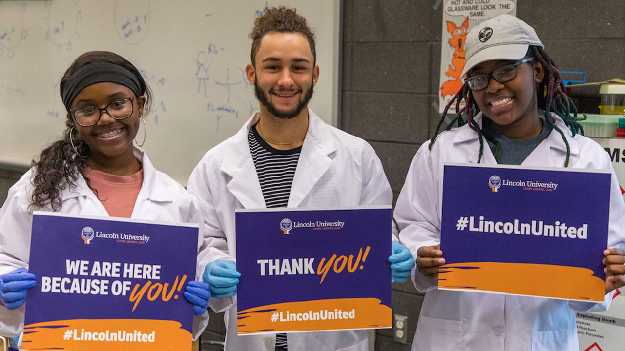 Three Lincoln University students smiling and holding signs saying "We are here because of you! #LincolnUnited".