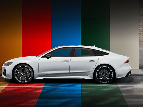 Side profile of a silver Audi RS 7 parked in front of a brightly-striped wall.