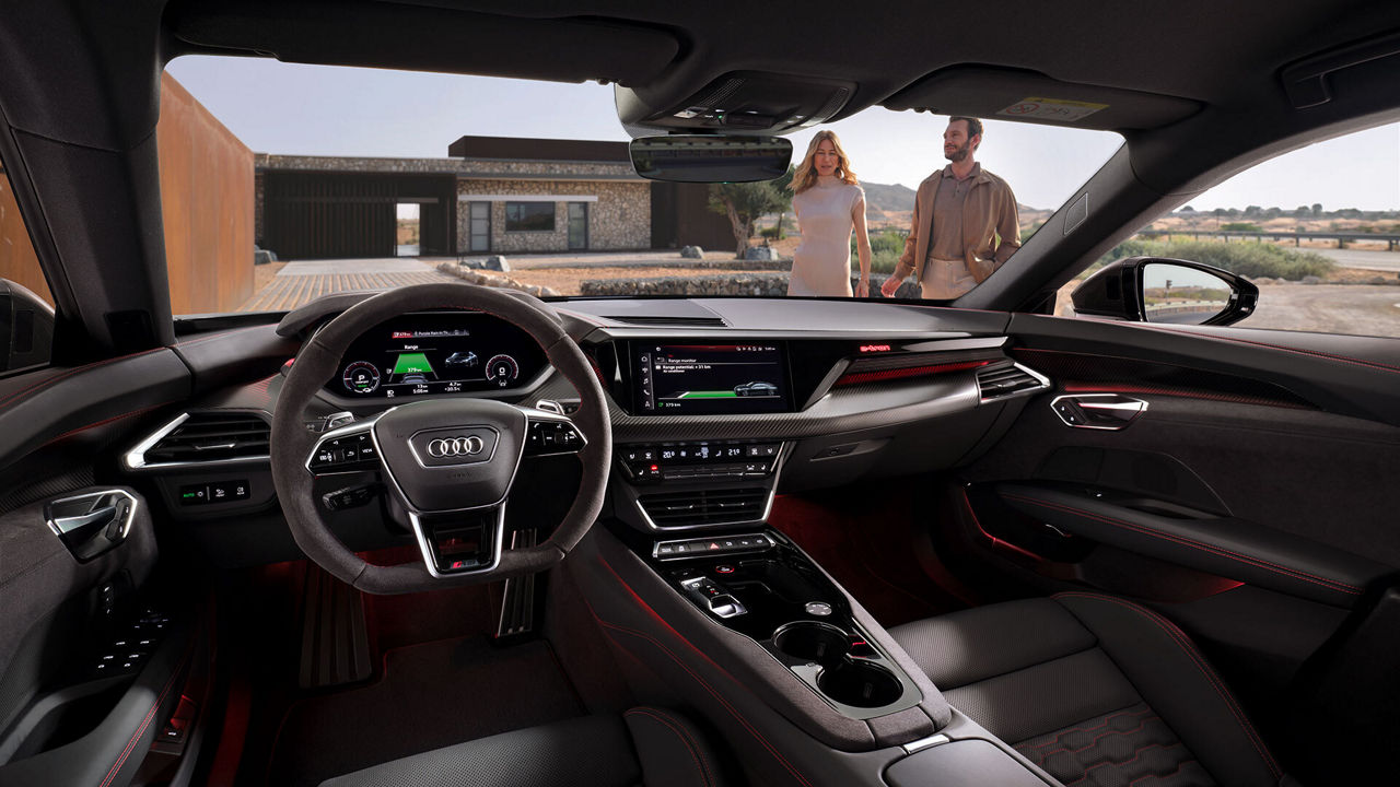 A man and woman approaching their Audi, viewed from the inside cockpit. 