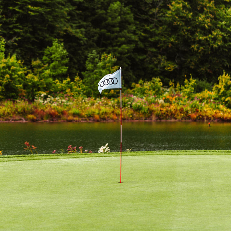 Close-up photo of an Audi golf flag on the green of a golf course.