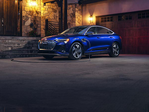 A blue Audi e-tron vehicle hooked up to a home charger.