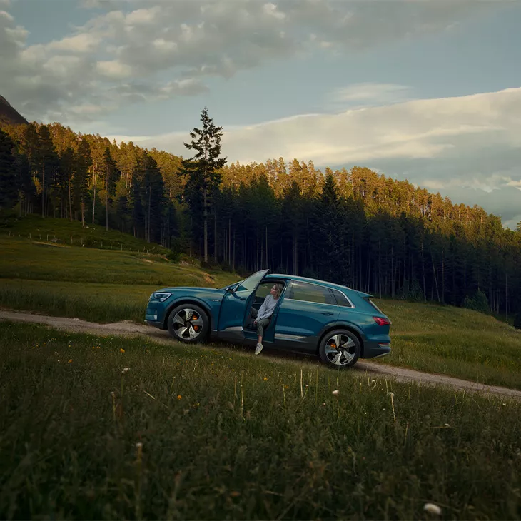 A woman sitting in her Audi e-tron parked on a hill. 