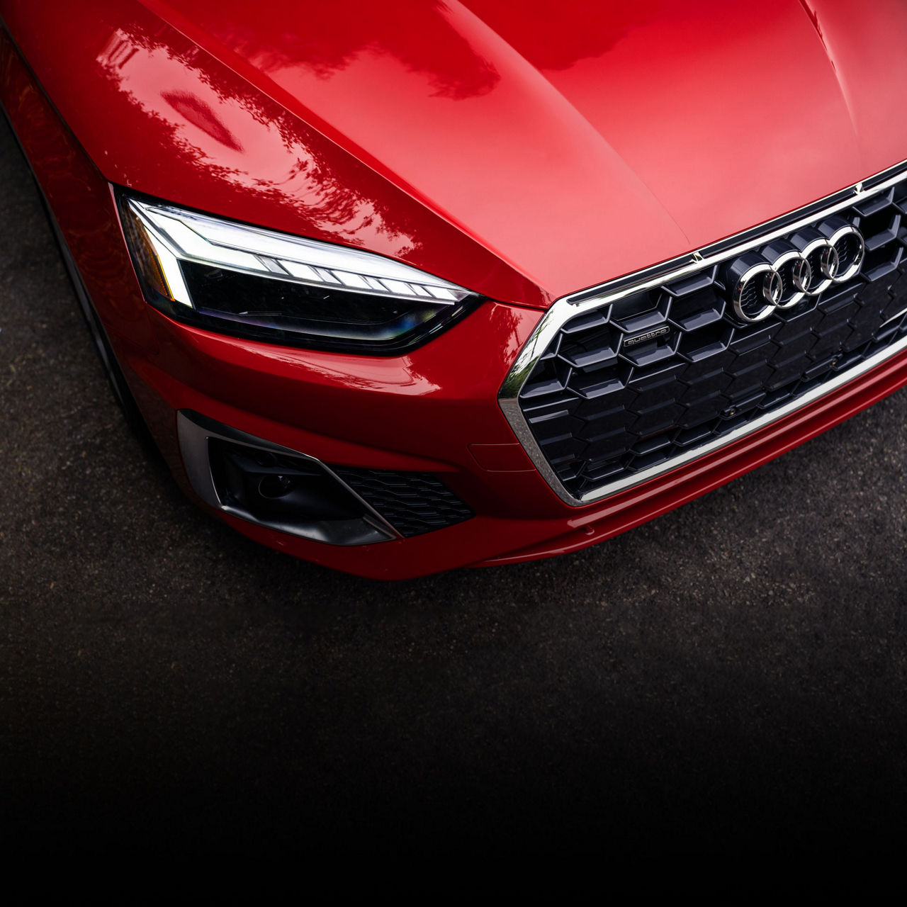 Close-up overhead view of the grille and headlights of a red Audi. 