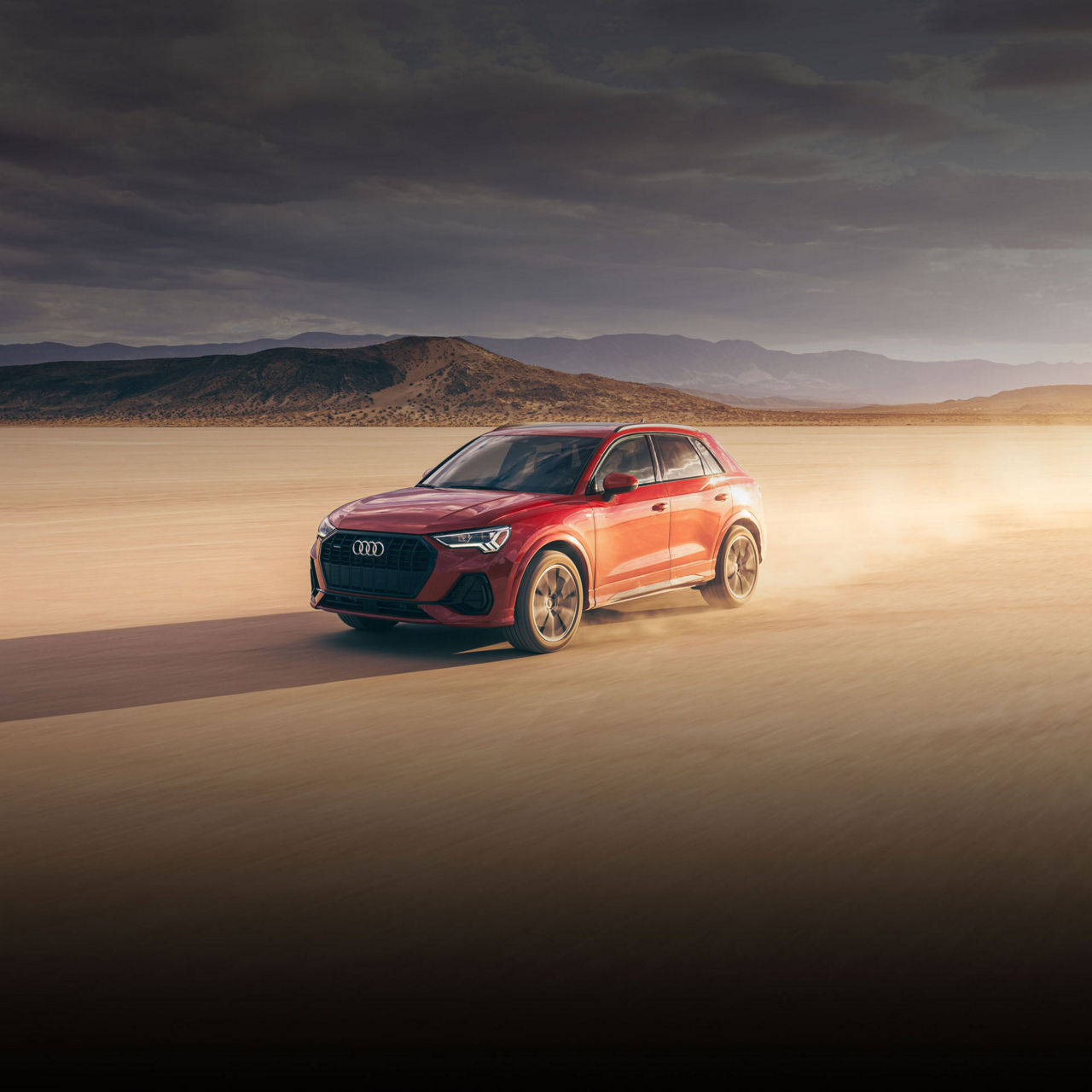 Three-quarter front view of a red Audi Q3 driving through a desert valley. 