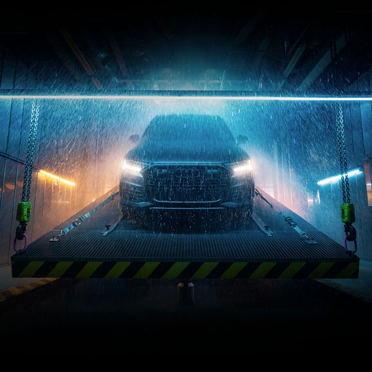 An Audi Q7 withstanding a simulated rainstorm on an inclined platform in a dark room. 