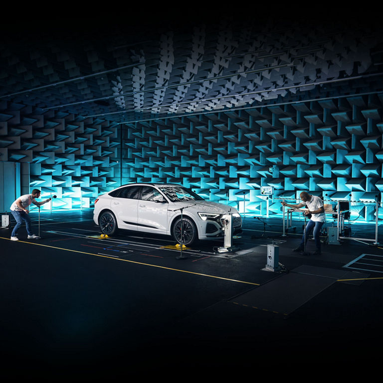 Two Audi technicians testing the interior sound-proofing of an Audi Q8 e-tron in a sound-proof testing room. 