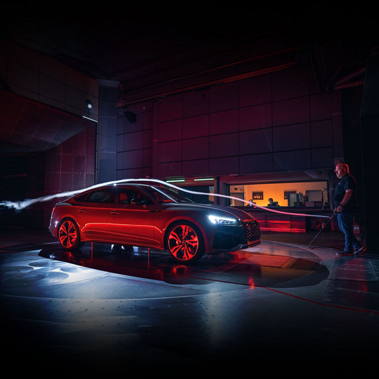 Three Audi technicians demonstrating the aerodynamics of an Audi A5 Sportback using illuminated air streams.  