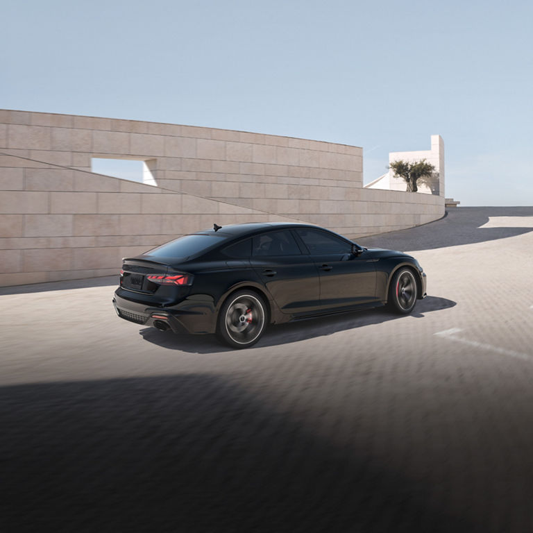 Three-quarter rear view of a black Audi RS 5 Sportback accelerating. 
