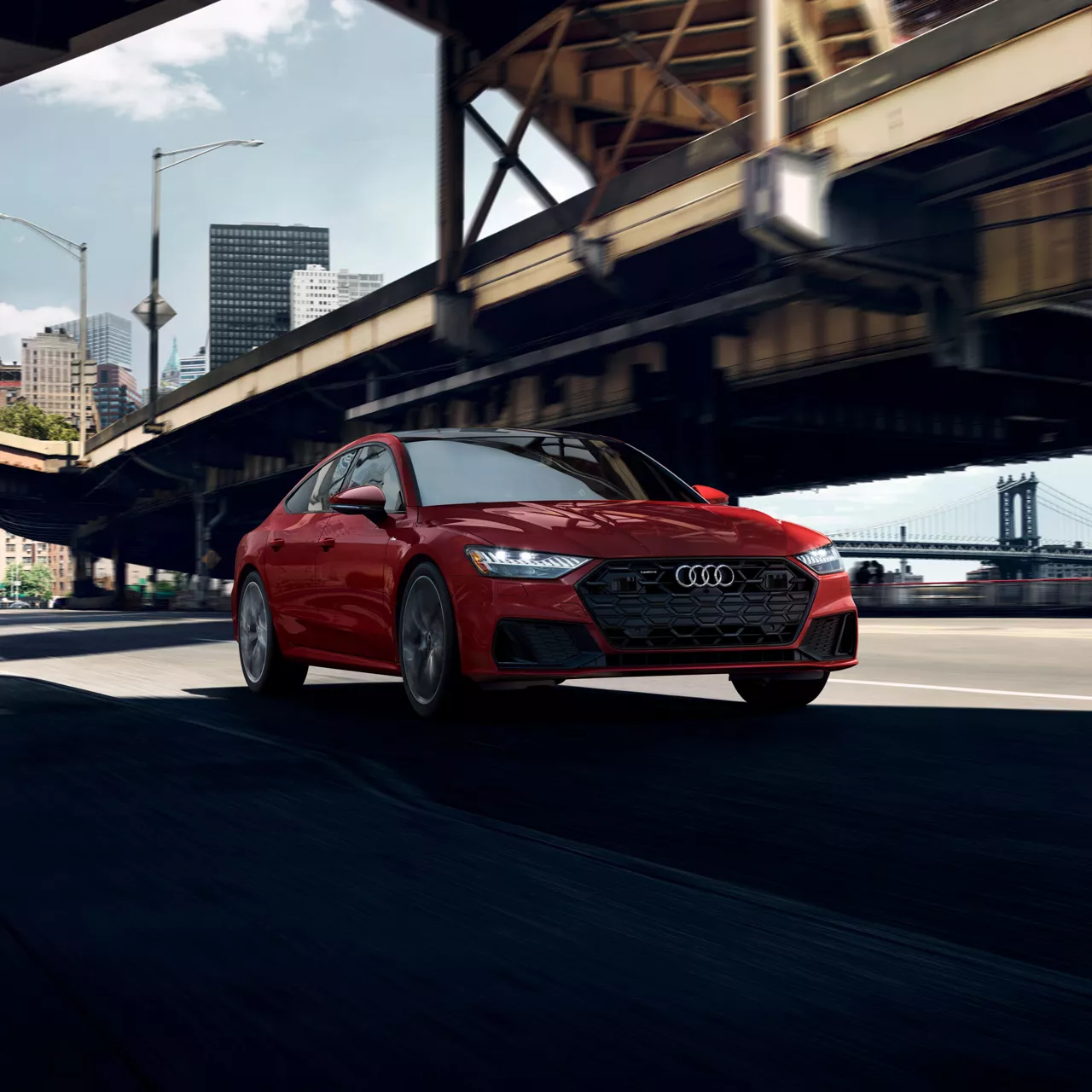 A red Audi A7 driving under a highway overpass. 