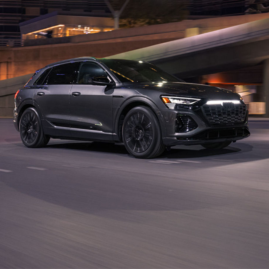 A grey Audi Q8 e-tron driving under a city overpass at night.