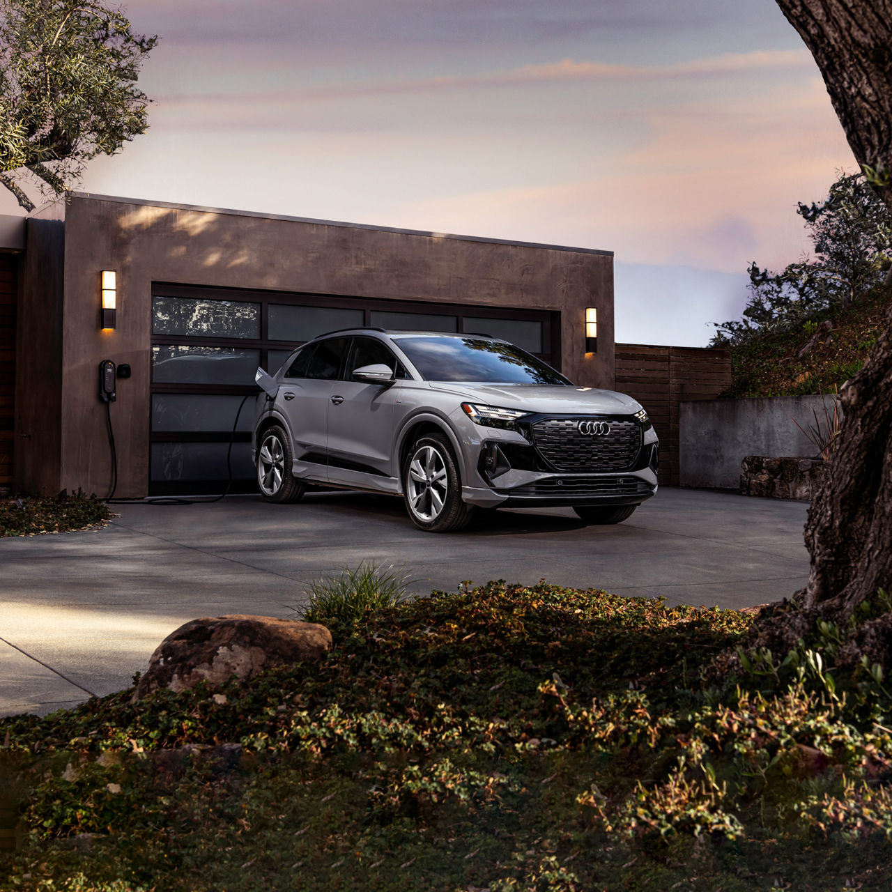 Three-quarter front-view of the Audi Q4 e-tron® charging in front of a person's home. 