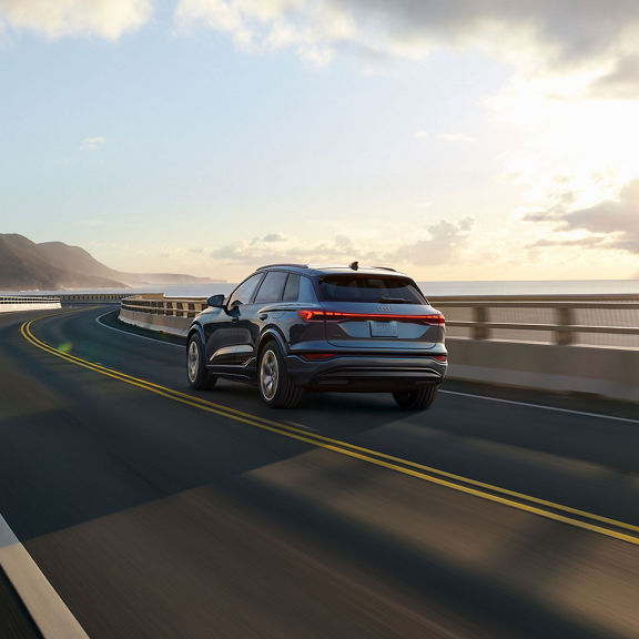 Three-quarter rear-view of the Audi Q6 e-tron accelerating on an oceanside road.