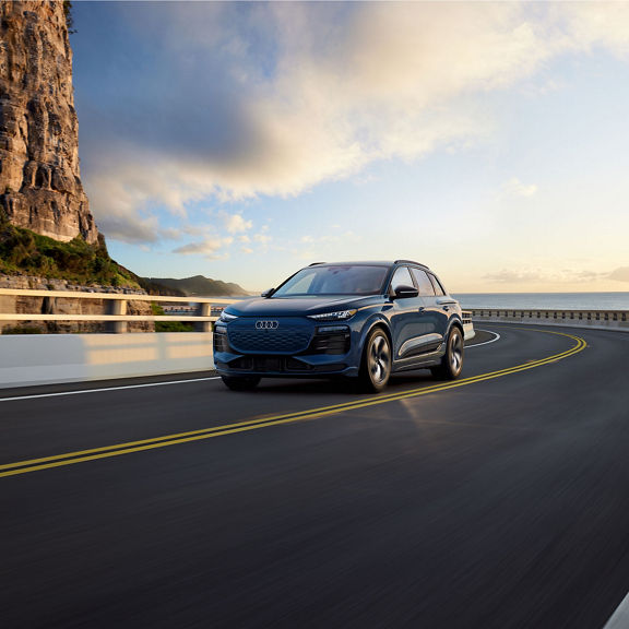 Three-quarter front-view of the Audi Q6 e-tron accelerating on an oceanside road.