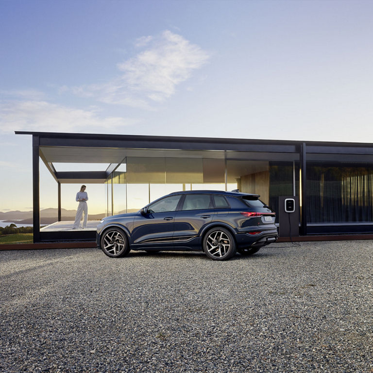 Three-quarter side view of the Audi Q6 e-tron parked in front of a modern building.
